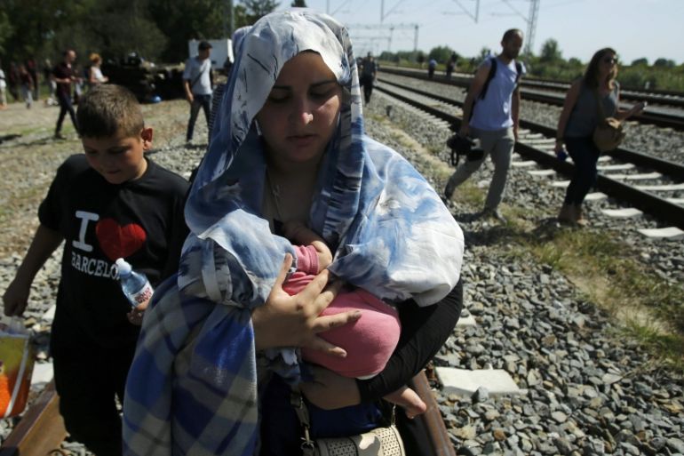 A migrant woman carries a baby as she walks on a railway track near Tovarnik
