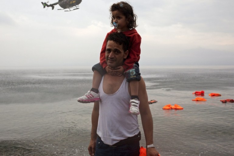 A Syrian refugee carries his daughter as a Frontex helicopter flies over on the Greek island of Lesbos