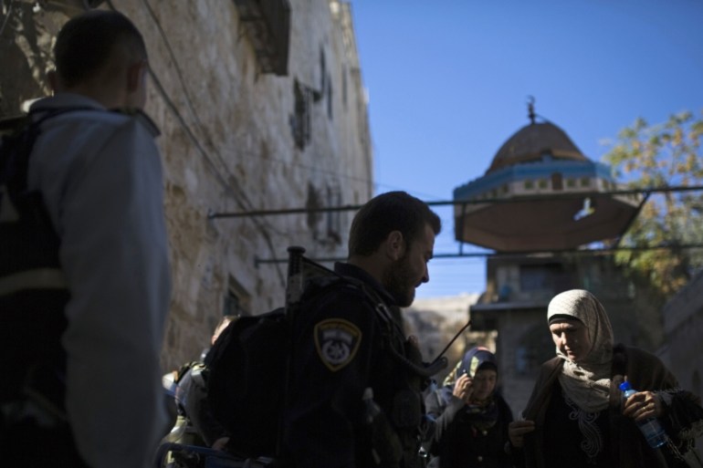 A Palestinian woman walks past an Israeli police officer near the Lions Gate in the Old City of Jerusalem before Friday prayers