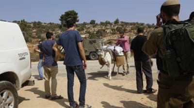 Israeli soldiers and Jewish settlers stand guard as a Palestinian farmer passes a road near Nablus City [Al Jazeera]