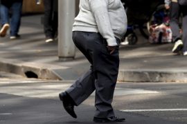 A man crosses a main road as pedestrians carrying food walk along the footpath in central Sydney, Australia
