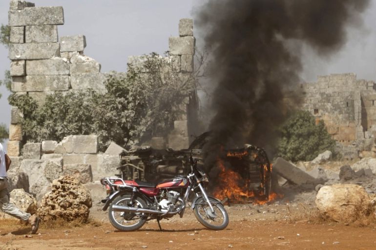 A man runs past a burning military vehicle at a base controlled by rebel fighters from the Ahrar al-Sham Movement in the southern countryside of Idlib