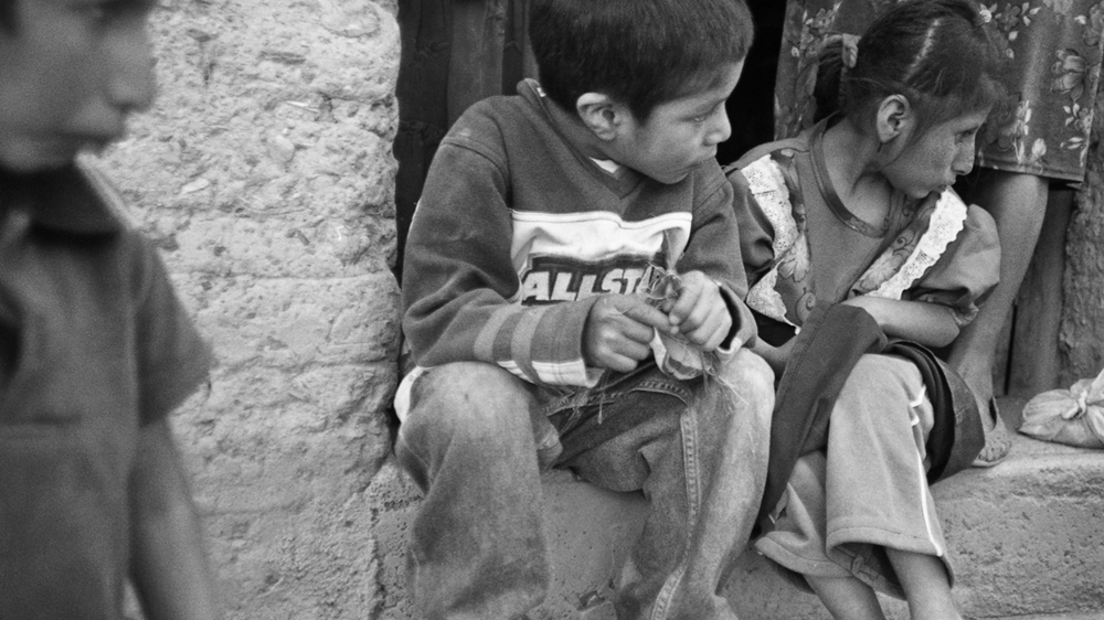 Children sit on a step. Agustín, left, and his cousin, on the right, are unable to walk or talk and are highly sensitive to sunlight [Prometeo Lucero]