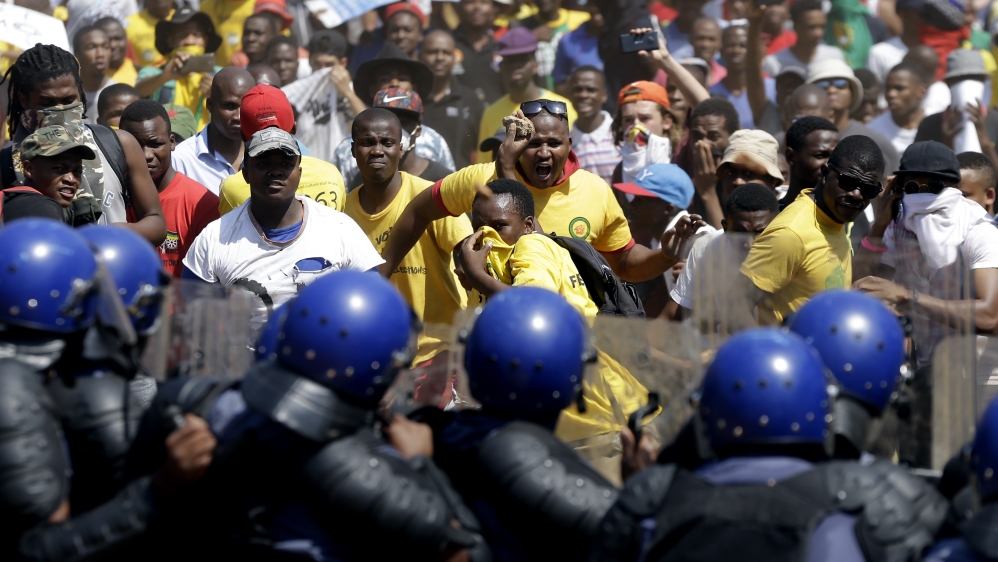 Students throw stones against riot police officers during their protest against university tuition hikes outside the union building in Pretoria on Friday [AP]