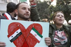 A pro-Syrian regime protester holds a placard showing the Iranian and Syrian flags during a protest in front the Iranian embassy in Damascus [AP]