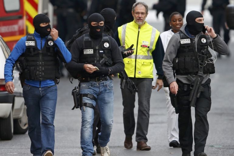 Masked French judicial police unit members walk at the scene of the raid in Saint-Denis