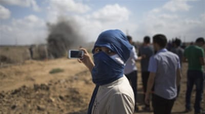 A Palestinian protester films with his mobile phone, during clashes with Israeli soldiers on the Israeli border of Gaza [AP]