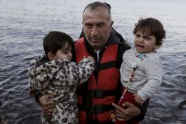 A migrant holds two children as refugees and migrants arrive on an overcrowded boat on the Greek island of Lesbos