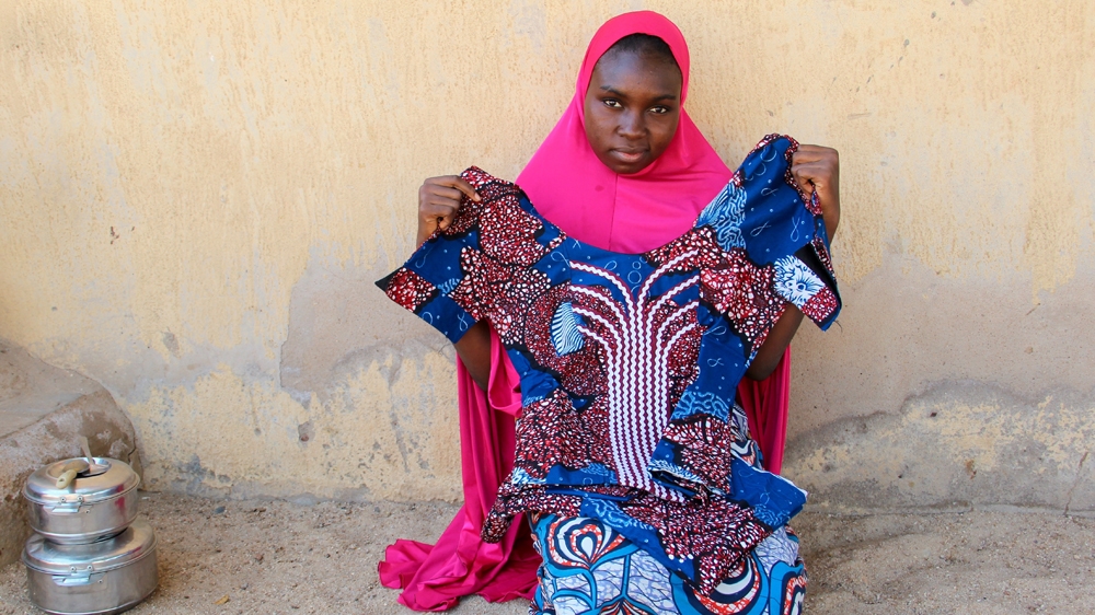 Aliyu's younger sister Habiba holds the outfit she had made from some cloth her brother gave her as a present [Femke van Zeijl/Al Jazeera] 