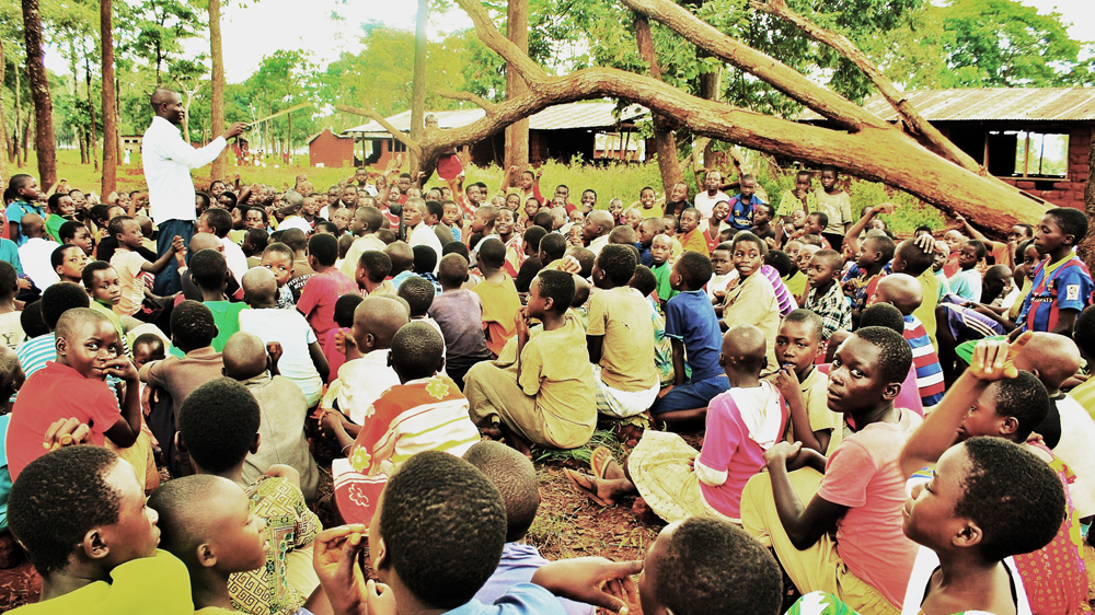 Early high school pupils attend an informal class under a tree at Nduta camp [Tendai Marima/Al Jazeera]