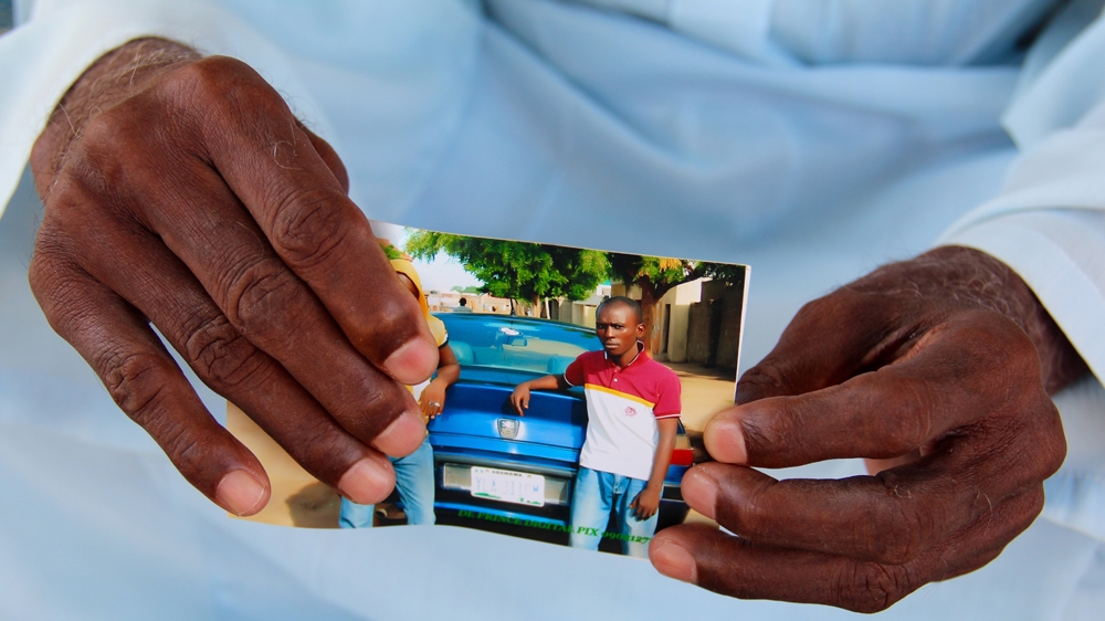 Aliyu's father Mohammed holds a recent picture of him taken in the street where the family lives [Femke van Zeijl/Al Jazeera] 