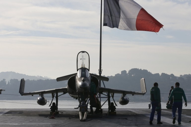 Flight deck crew work around a Super Etendard fighter jet as a French flag flies aboard the French nuclear-powered aircraft carrier Charles de Gaulle before its departure from the naval base of Toulon