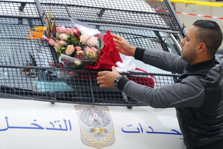 A man places a bouquet of flowers on a police van, near the bus that exploded Tuesday in Tunis [AP]