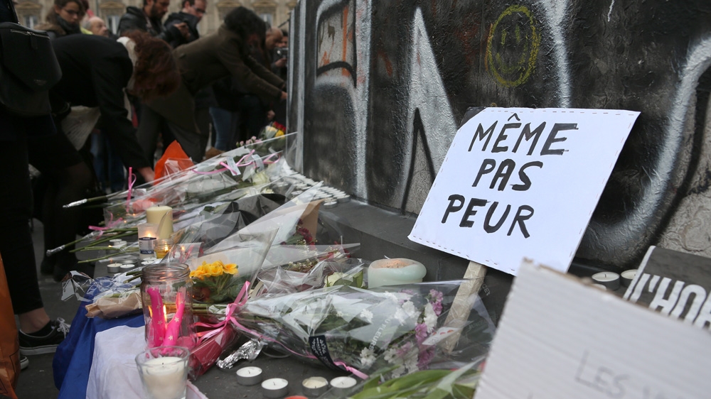 A placard reads 'Not even scared' amid the flowers and candles at the Republique Square, the day after the Paris attacks [Maya Vidon-White/Al Jazeera]
