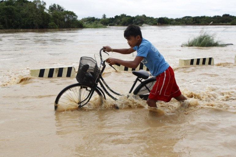 A boy pushes his bicycle through a flooded road after heavy rain at Candaba town