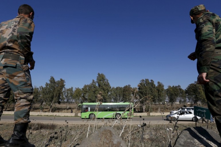 Syrian Army forces look on as buses leave district of Waer during a truce between the government and rebels, in Homs