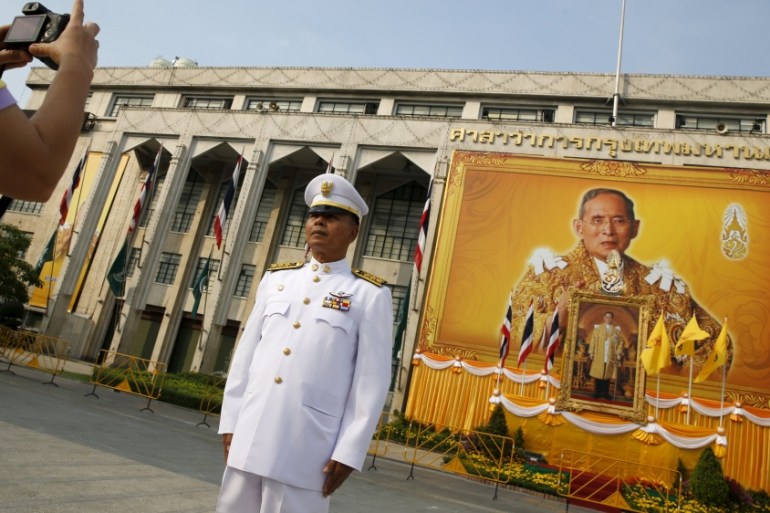 An army official takes a picture of him in front of of Thai King Bhumibol Adulyadej pictures as people gather to mark his 88th birthday in Bangkok