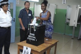 A police officer and an election official watch as a voter cast her ballot in the presidential polls in Victoria, Seychelles