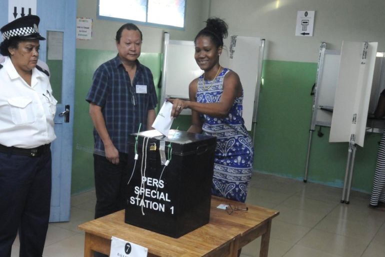 A police officer and an election official watch as a voter cast her ballot in the presidential polls in Victoria, Seychelles