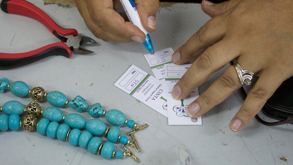 Daria tags a bead bracelet she’s made for sale. Refugees in Malaysia aren’t legally allowed to work [Al Jazeera]