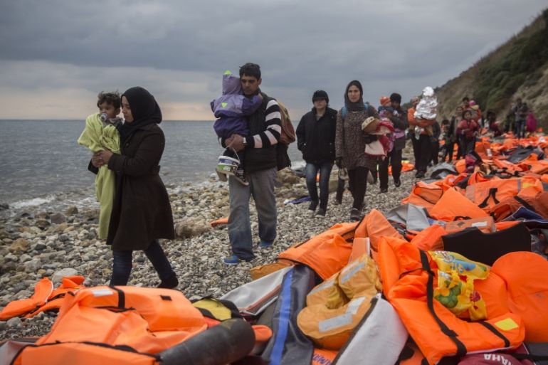 Refugees and migrants walk along a beach after crossing a part of the Aegean