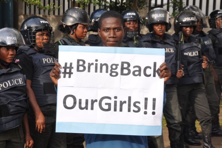 man poses with a sign in front of police officers in riot gear during a demonstration calling on the government to rescue the kidnapped girls of the government secondary school in Chibok
