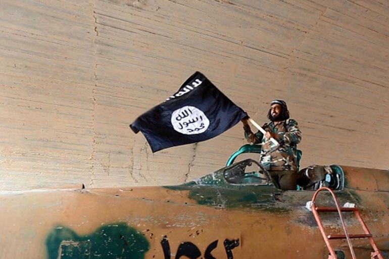 ISIL fighter waving a flag while standing on captured government fighter jet in Raqqa, Syria [Getty]