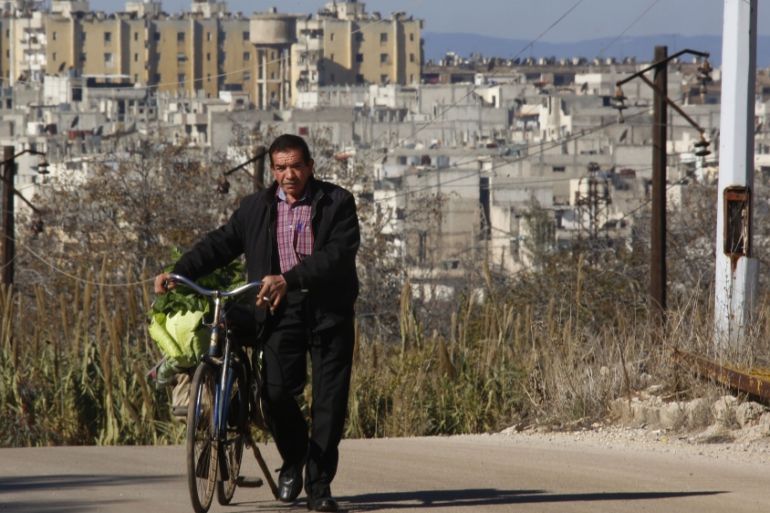 A man is seen pushing his bicycle in an area adjacent to the Waer neighborhood in the central city of Homs, Syria [AP]