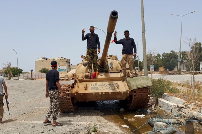 Members of the Libyan pro-government forces gesture as they stand on a tank in Benghazi