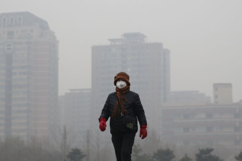 A woman wearing a protective mask takes a walk at a park in the morning on an extremely polluted day in Beijing