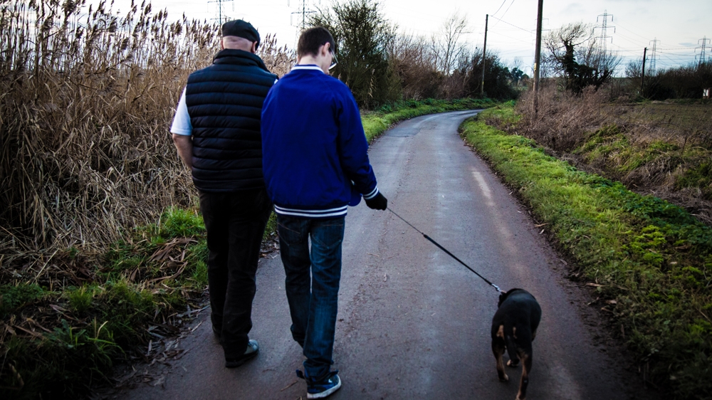 Paul, left, and Harry Jackson take the family dog for a walk. Harry was four years old when Sharon and Paul adopted him and his two sisters. He has been diagnosed with Alcohol-Related Neurodevelopmental Disorder (ARND) and, like all of his siblings, has at times been excluded from school for bad behaviour [Michael Mowbray/Al Jazeera] 