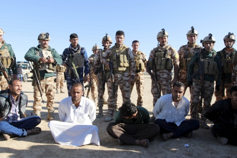 Kurdish peshmerga forces stand near detained men, who they suspect of being linked to an attack on the outskirts of a town northwest of Kirkuk [REUTERS]