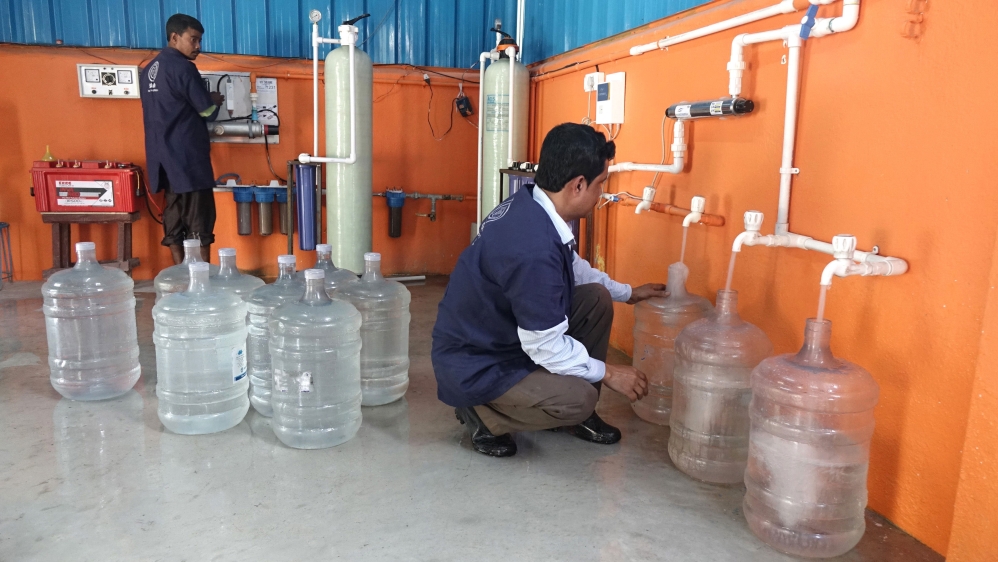 Inside the Sulabh Water plant at Madhusudankati. Workers collect treated pond water in refillable jars. The plant produces 4,000 litres of treated potable water every day [Shaikh Azizur Rahman/Al Jazeera]