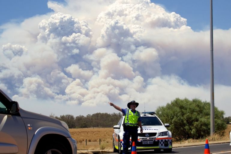Smoke clouds from a large bush fire are seen behind a police road block at the turn off onto the South Western Highway near Pinjarra, Western Australia