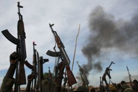 Rebel fighters hold up their rifles as they walk in front of a bushfire in a rebel-controlled territory in Upper Nile State