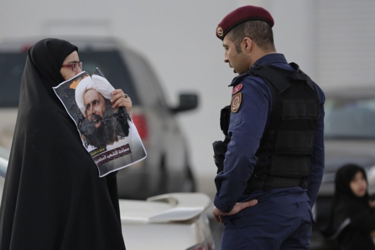 A Bahraini protester holds up a picture of Saudi Shiite cleric Sheikh Nimr al-Nimr toward a riot police officer in Daih