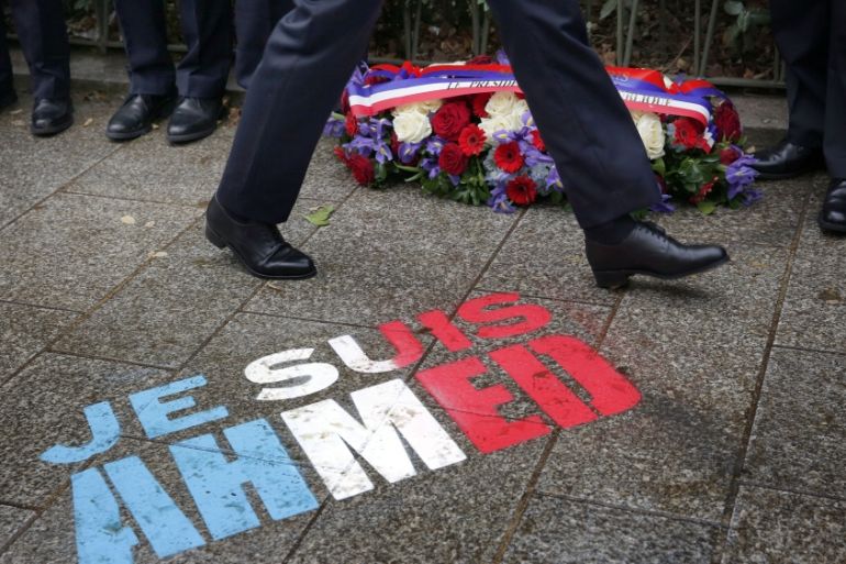 Policemen walk past spray painted on the sidewalk reading: "Je suis Ahmed," in the red, white and blue of the French flag near a plaque commemorating late police officer Ahmed Merabet in Paris [AP]