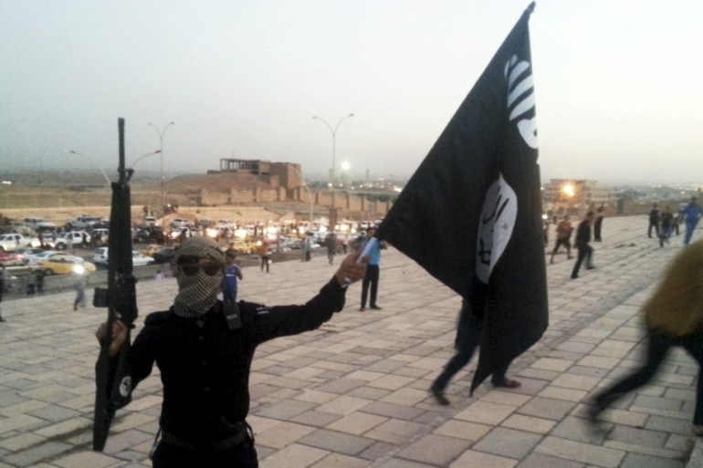 An ISIL fighter holds an ISIL flag and a weapon on a street in the city of Mosul, Iraq [REUTERS]