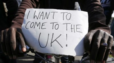 A migrant holds a placard on his bicycle at a makeshift camp in Calais, France [REUTERS]