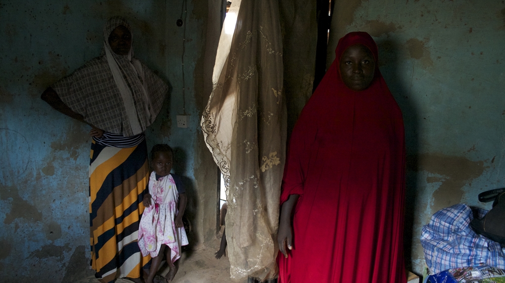 Nguru, with her belongings piled in the corner of the room where she helps the women deliver, and a neighbour standing beside her [Caelainn Hogan/Al Jazeera]