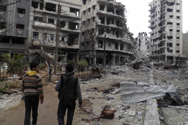 Free Syrian Army fighters walk along a deserted street past damaged buildings in the besieged area of Homs