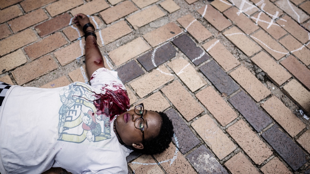 A Wits protester smeared in fake blood pretends to be dead as a commentary on the university killing the future of poor South Africans who cannot afford their fees [Cornel van Heerden/Al Jazeera]