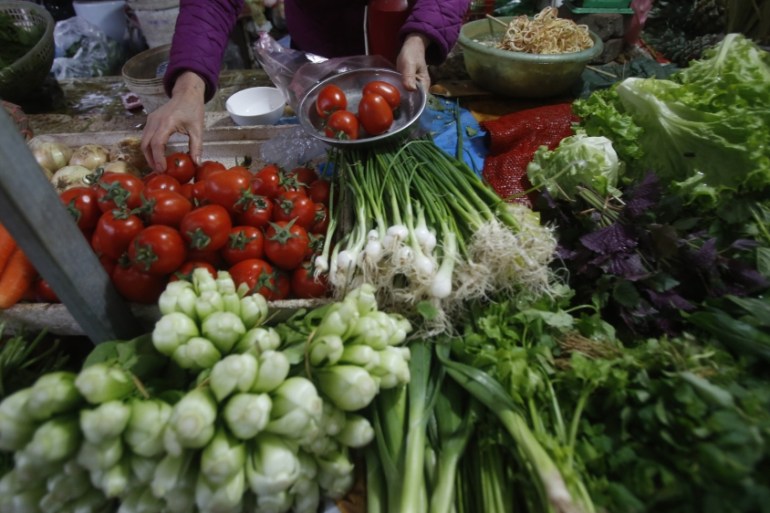 A food and vegetable seller weights tomato at a market in Hanoi