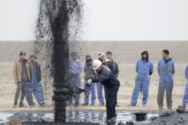 Iraqi workers stand near a pipeline as it ejects oil at Al Tuba oil field in Basra
