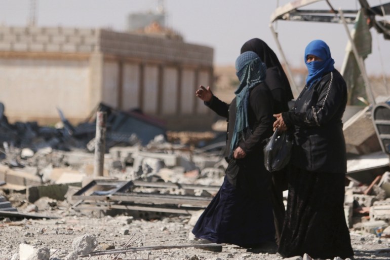 Women walk on rubble in al-Shadadi town, in Hasaka province