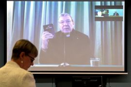 Senior Counsel Assisting Gail Furness stands in front of a screen displaying Australian Cardinal George Pell as he holds a bible while appearing via video link from a hotel in Rome, Italy t