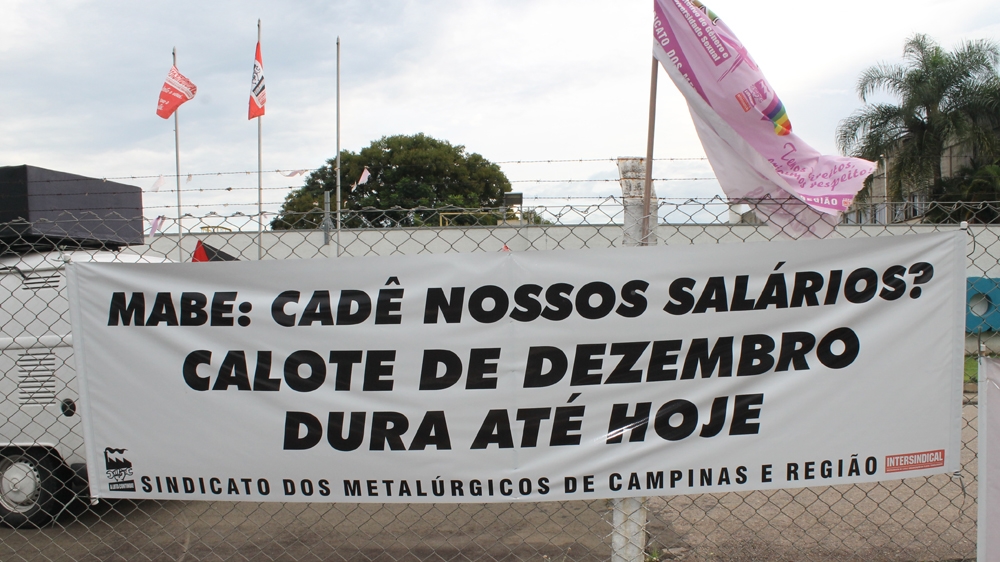 A sign reads: 'Mabe, where are our salaries?' [Sam Cowie/Al Jazeera]