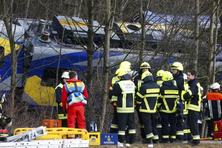 Members of emergency services stand next to a crashed train near Bad Aibling