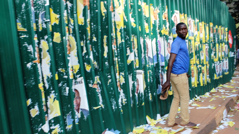 A tattered campaign: An opposition supporter walks past posters of President Yoweri Museveni that have been defaced by students [Tendai Marima/Al Jazeera]
