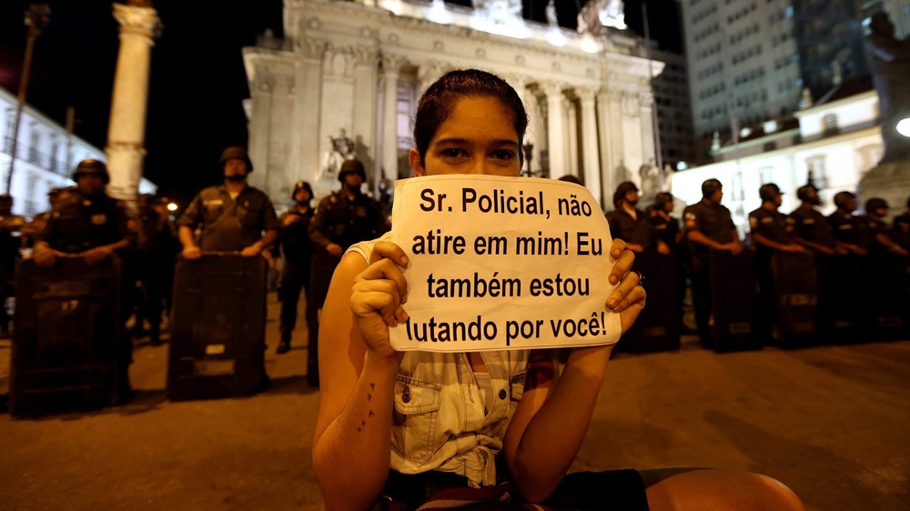 A woman holds a poster reading 'Mister policeman, don't shoot at me, I'm fighting for you too' as people demonstrate in front of policemen during a protest to demand better funding for health and education in Rio de Janeiro in June 2013. Doctors say the healthcare crisis has been a long time in the making [EPA/MARCELO SAYAO]